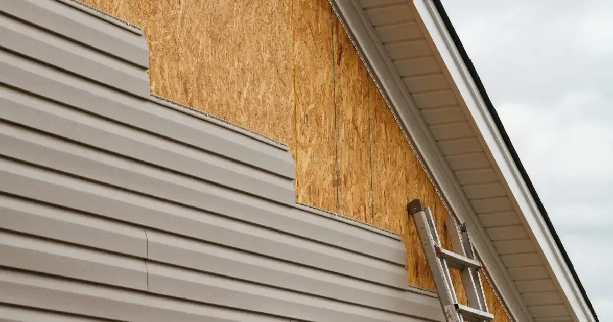 A home with PVC-coated aluminum trim partially installed, with the top-right portion of the home showing plywood underneath