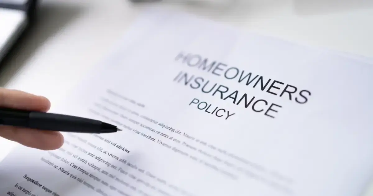 A hand holding a pen over a homeowner's insurance policy document