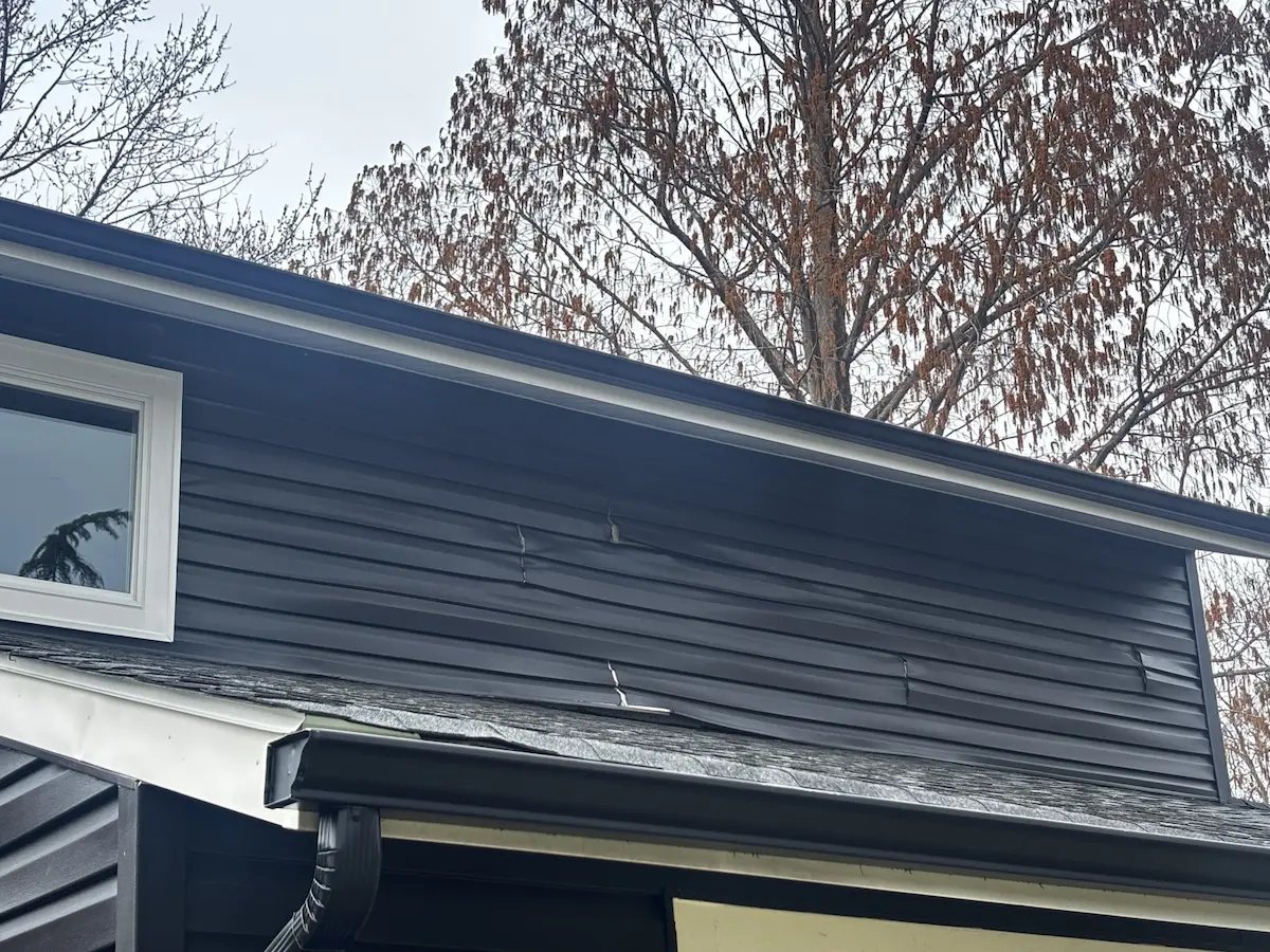 Photo showing warped and buckled vinyl siding on a house due to excessive heat from painting old siding a dark color without proper UV protection.